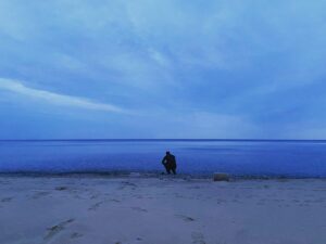 person crouching by a large lake
